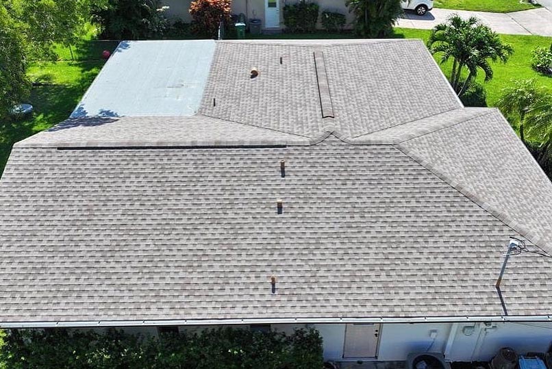A house with a shingle roof, green lawns, and trees.